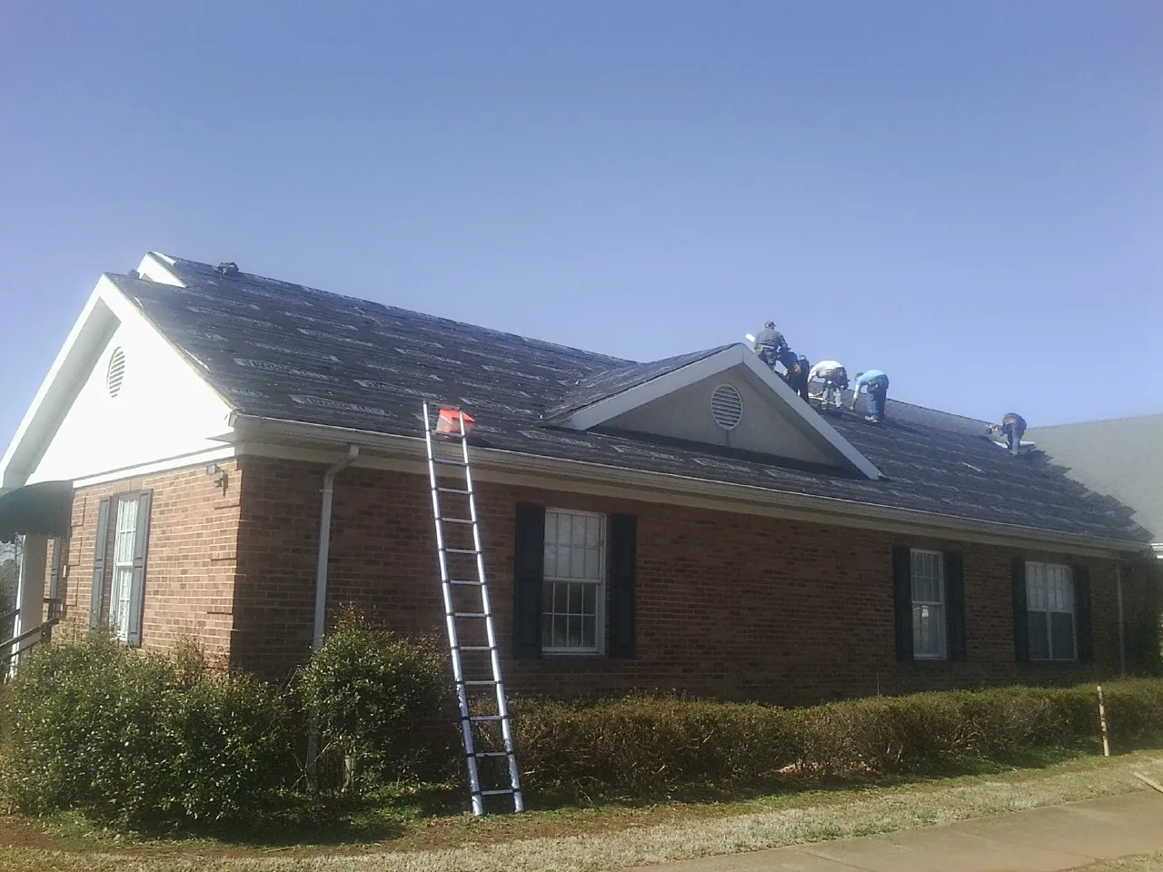 Crew tearing shingles off a brick ranch roof with a ladder set — Metal Roof Repair work by our crew in Faith