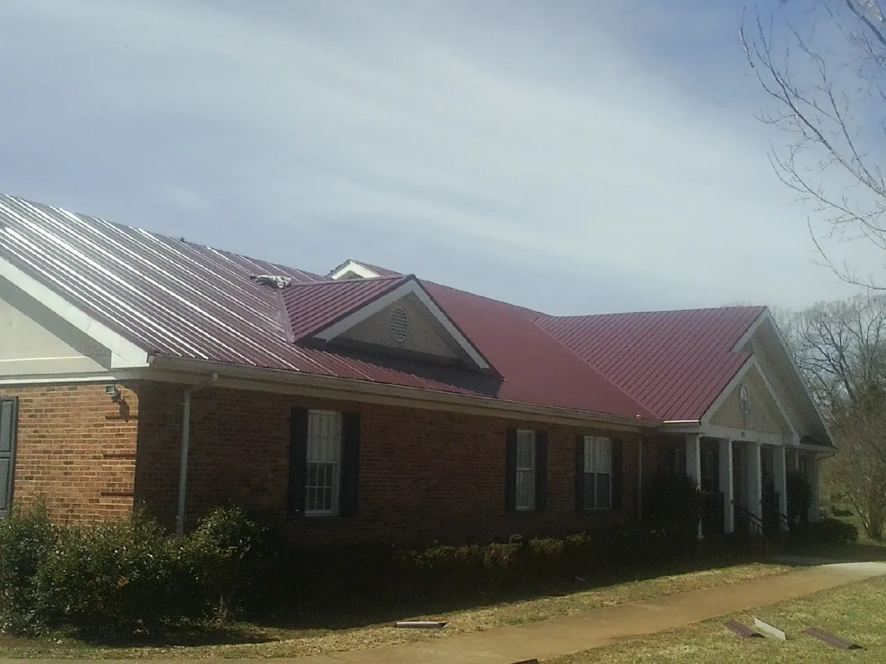 Red metal roof with gabled entries on a long brick building, from a Hail Damage Roof Repair job in Faith