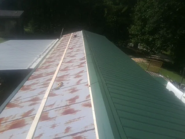 Old rusted panels beside newly installed green metal roofing — Wind Damage Roof Repair by Roofing Brothers in Faith