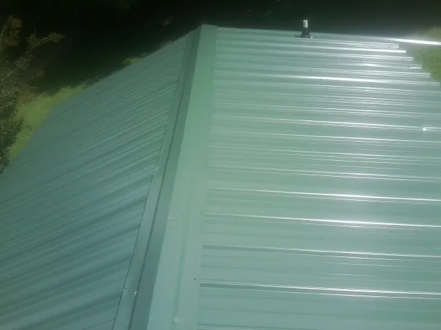 New green metal panels meeting at the ridge of a roof — Flat Roof Repair work by our crew in Faith