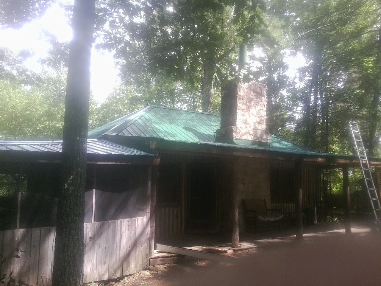 Green metal roof and stone chimney above a log cabin porch in Faith