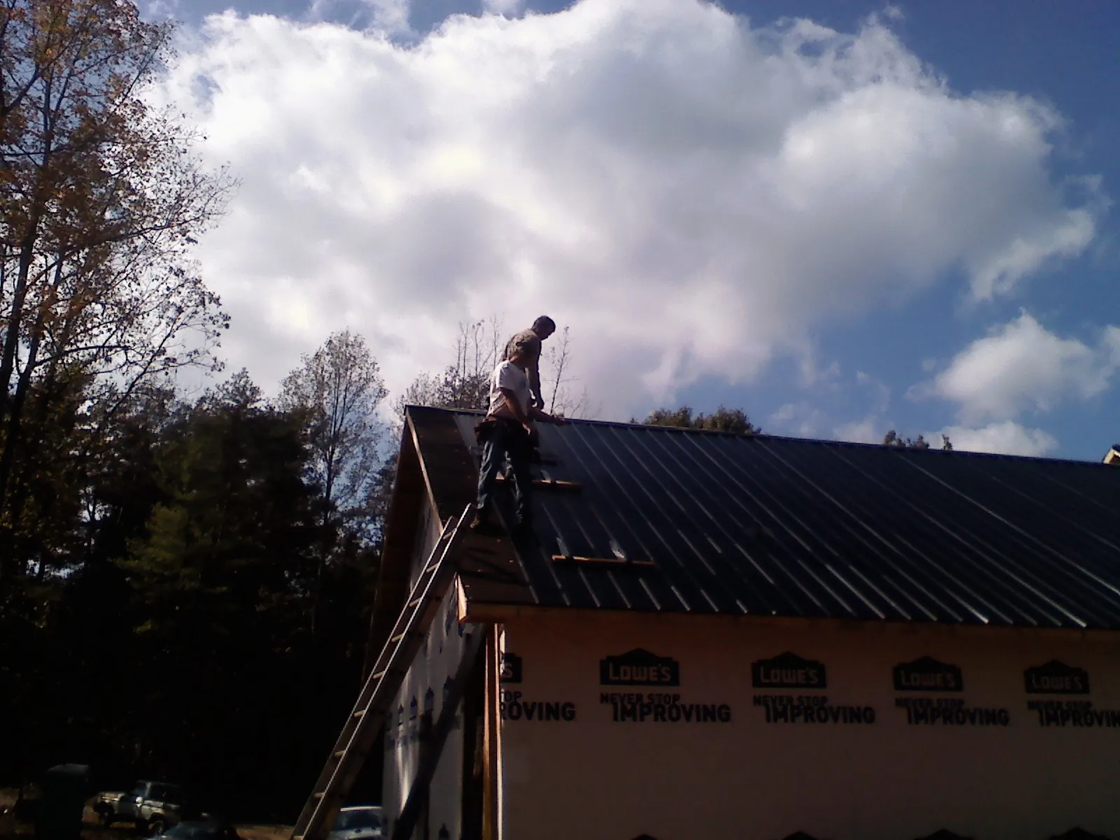 Roofer fastening dark metal panels high against a cloudy sky, from a Roof Inspection job in Faith