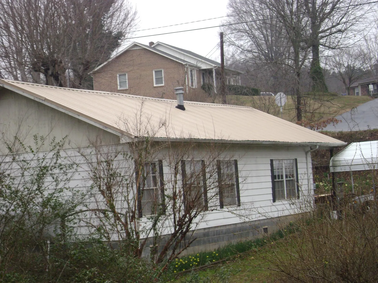 Tan metal roof on a white sided house set into a hillside — Commercial Roofing by Roofing Brothers in Faith