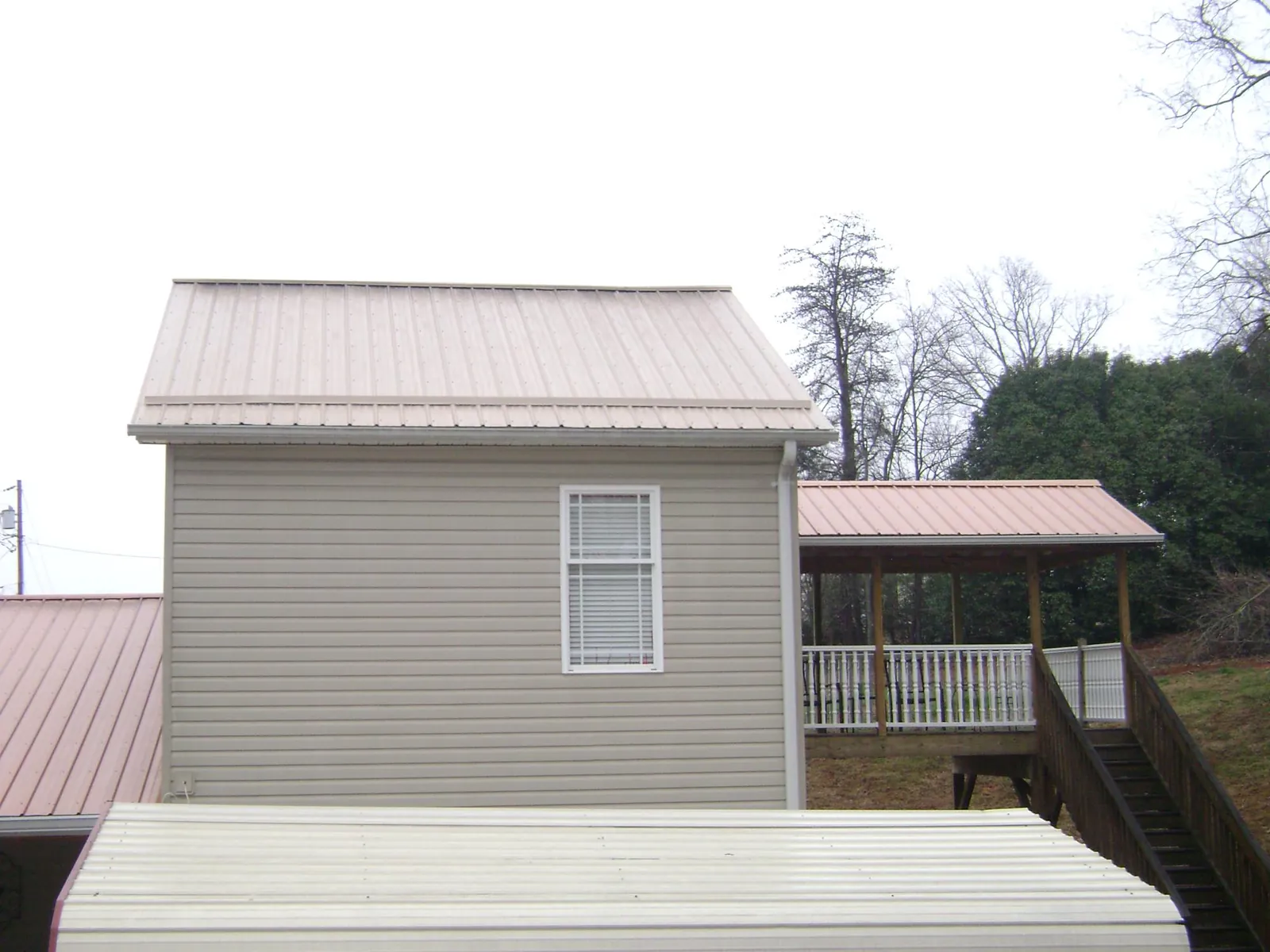 Tan metal roofs on a two story addition and attached porch, from a Roof Replacement job in Faith
